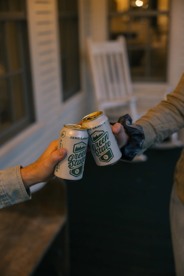 Two guests clinking canned drinks on the porch in the evening